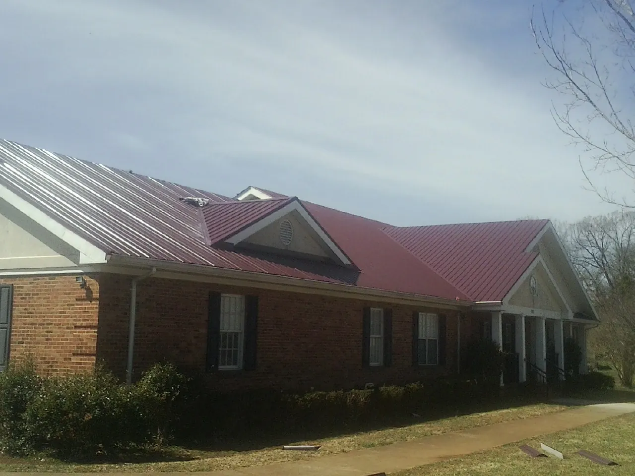 Red metal roof with gabled entries on a long brick building, from a Hail Damage Roof Repair job in Hawley