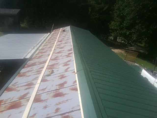 Old rusted panels beside newly installed green metal roofing — Wind Damage Roof Repair by Roofing Brothers in Hawley