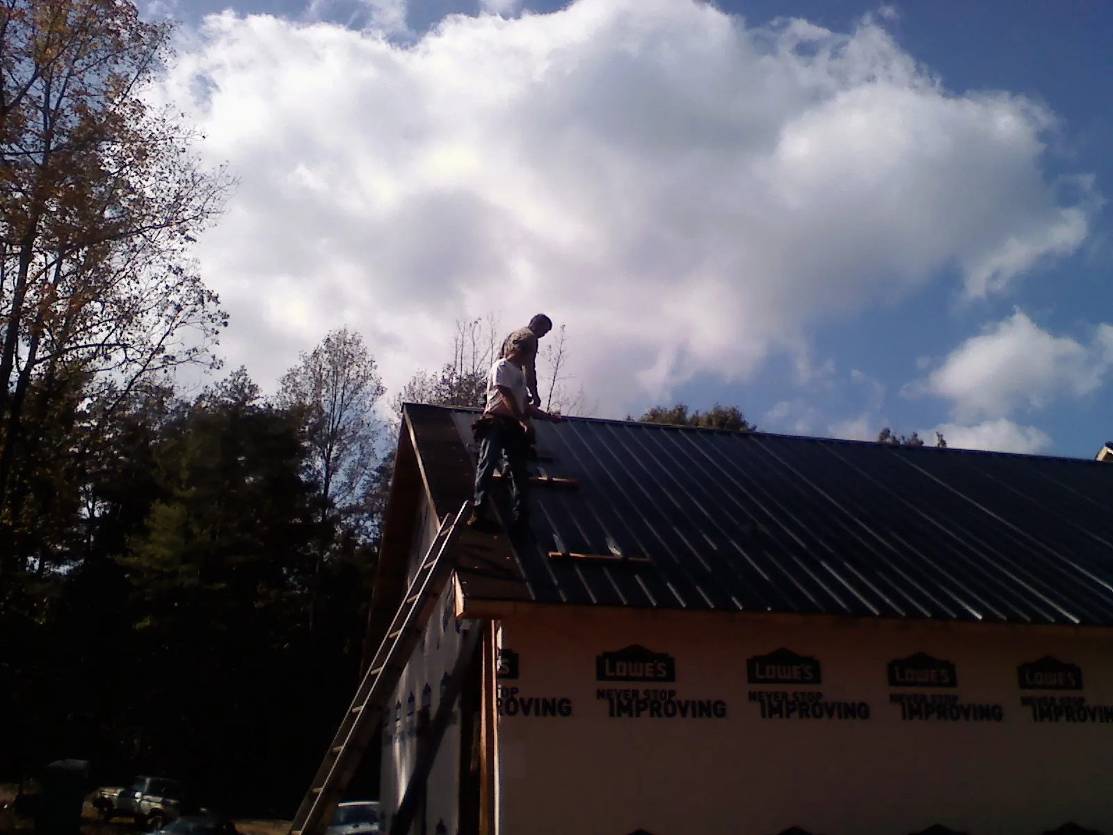 Roofer fastening dark metal panels high against a cloudy sky, from a Roof Inspection job in Hawley